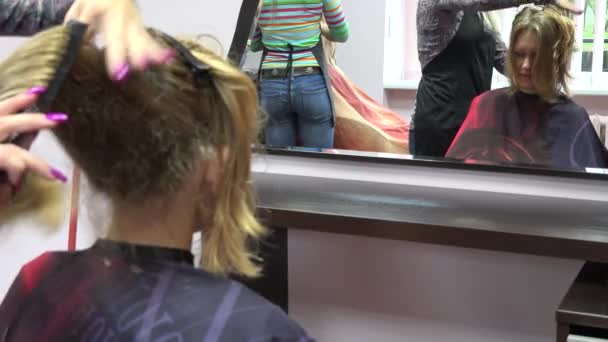 美容師は、鏡の前で女性客の髪をとかします。フォーカスの変更。4 k — ストック動画