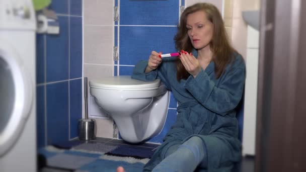 Беспокойная женщина смотрит на тест на беременность в ванной комнате . — стоковое видео