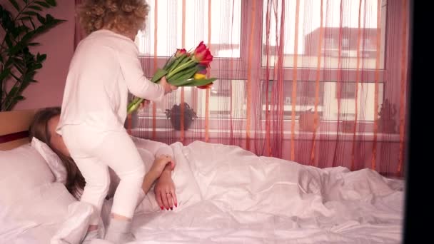 Carino bambina dando fiori alla mamma a letto il giorno delle madri — Video Stock