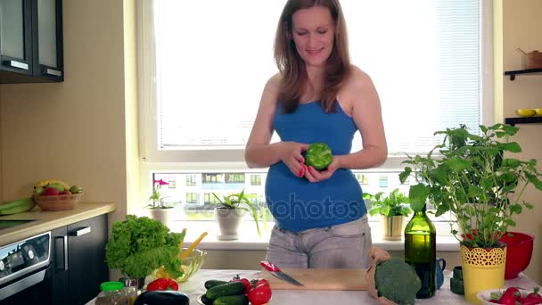 Terhesség és a táplálkozás. Terhes nő vágott paprika zöldségeket a konyhába asztal — Stock videók