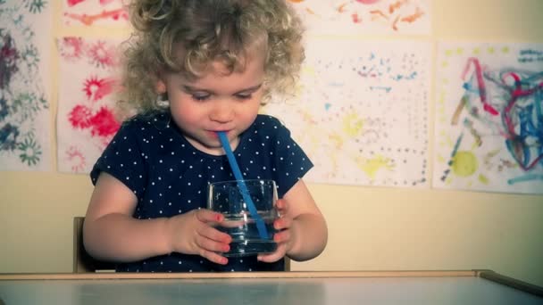 Pequeño niño lindo soplar aire a través de paja en vidrio con agua — Vídeo de stock