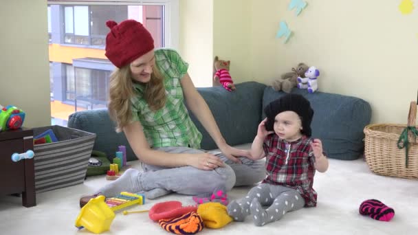 Madre joven con niña linda probar sombreros de punto caliente. 4K — Vídeos de Stock