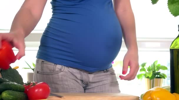 Estômago menina grávida e mãos cortando frutas páprica vermelha com faca para salada — Vídeo de Stock