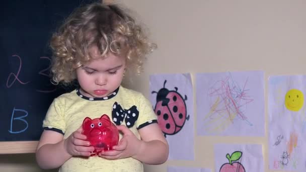 Linda menina sacudindo porquinho banco com moedas nele — Vídeo de Stock