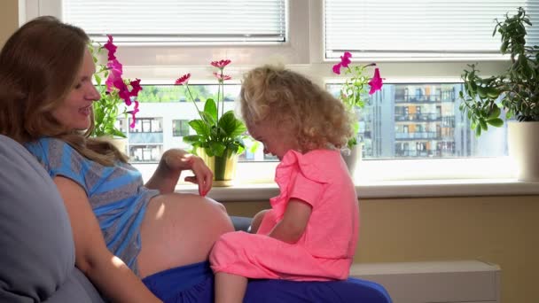 Kaukasiska gravid kvinna och Söt blond dotter flicka som leker med magen hemma — Stockvideo