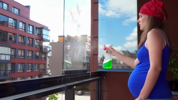 De schone ruit zwangere vrouwelijke vrouw met doek en reinigingsmiddel spray op eigen balkon — Stockvideo