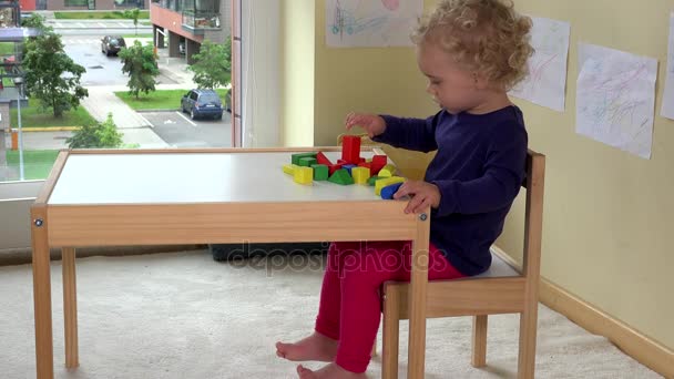 Маленька дівчинка грає з дерев'яними цегляними іграшками біля столу вдома — стокове відео