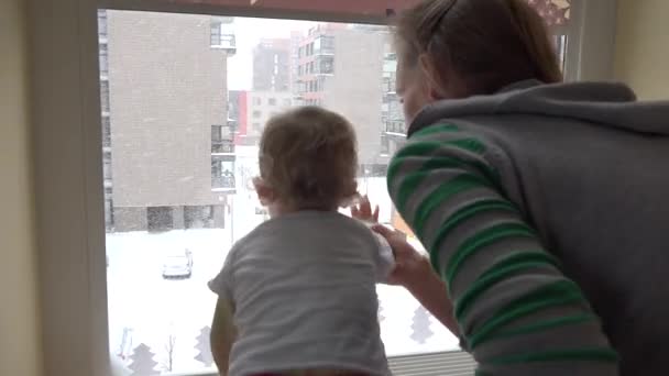 Kind mit Mutter beobachtet durch Fenster, wie es schneit. Kindheit. 4k — Stockvideo