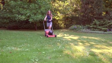 Kadın kadın çim biçme makinesi ile hareket eder ve yeşil çim mows. 4k