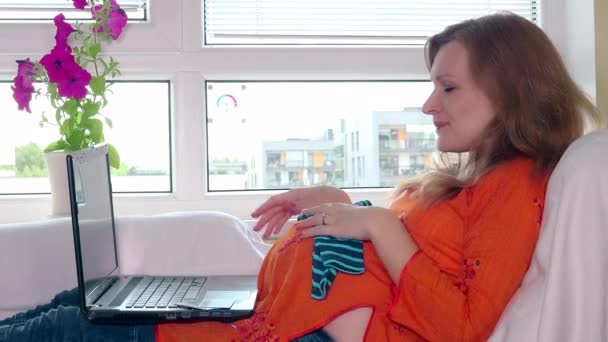 Pregnant woman with laptop computer and credit card shopping baby clothes online — Stock Video