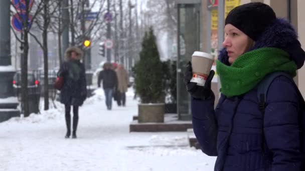 Mujer beber taza de té de café bebida caliente en ventisca de nieve y transeúntes ciudadanos — Vídeos de Stock