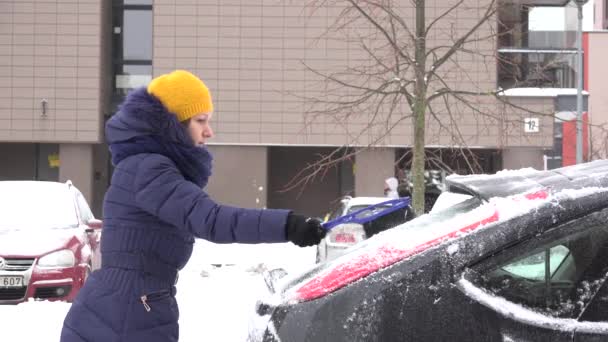 Frau reinigen schneebedecktes Auto mit Bürste in der kalten Winterzeit. 4k — Stockvideo