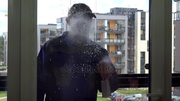 Male worker in blue uniform spray and wipe window with wiper tool. — Stock Video