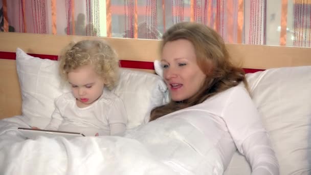 Pretty mom fall asleep while daughter girl play with tablet computer in bed — Stock Video