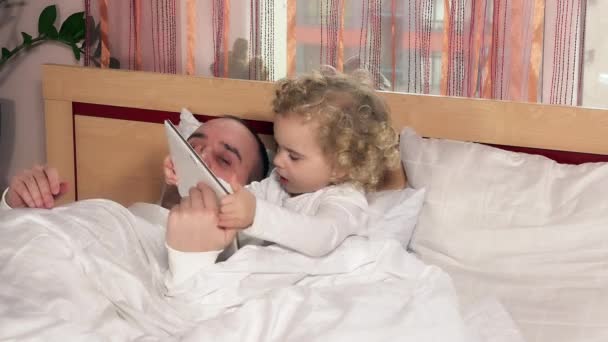 Лысый папа засыпает, пока дочь девочка играет с планшетным компьютером сидеть в постели — стоковое видео
