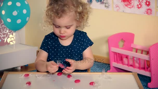 Enfant déballer des bonbons bonbons bonbons du papier et goûtez-le avec la langue sur la table . — Video