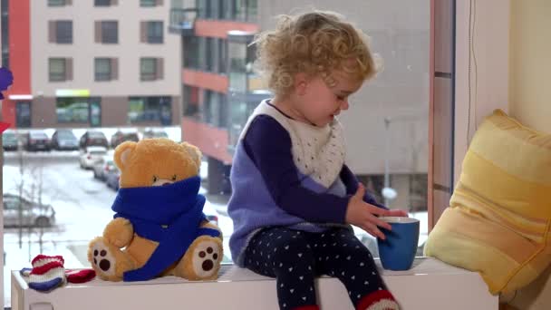 Freche Kind Junge mit Teetasse und bester Freund Teddybär sitzt auf Heizkörper — Stockvideo