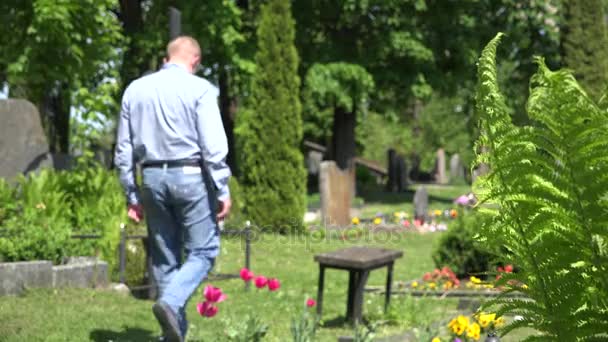 O homem solitário senta-se no banco à cruz de mármore no cemitério rural. 4K — Vídeo de Stock