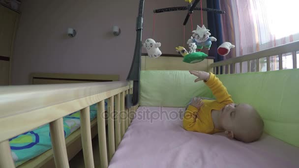 Bonito bebê jogar com carrossel na cama e rolar na barriga. 4K — Vídeo de Stock