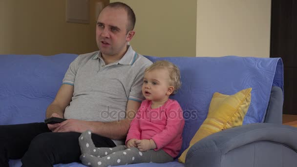 Père regarder la télévision avec petite fille douce assis à l'intérieur sur le canapé. 4K — Video