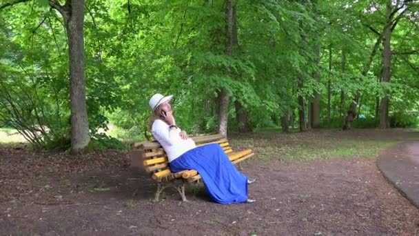 동안 공원 벤치 야외에 앉아 휴대 전화에서 기대 하는 어머니 이야기 — 비디오