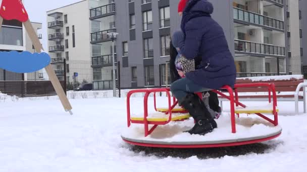 Familia con el pequeño columpio del juego del bebé en el patio de recreo en invierno. 4K — Vídeo de stock