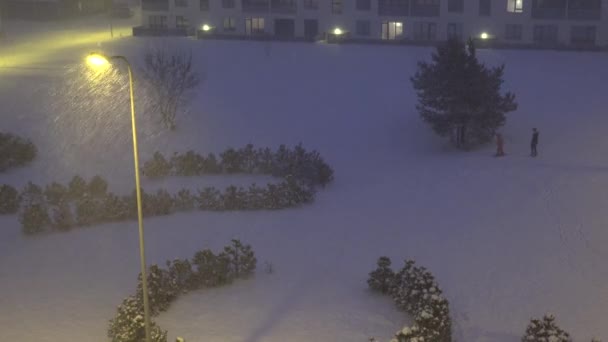 Fuertes tormentas de nieve caen en el distrito de casas vivientes por la noche y la gente. 4K — Vídeo de stock