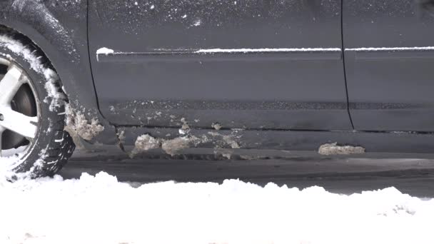 Человек стряхивает снег со снежных ног перед тем, как сесть в машину и закрыть дверь. 4K — стоковое видео