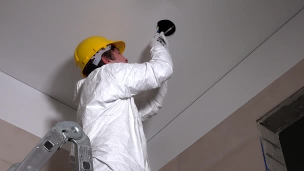 Trabajador masculino con agujeros cortados en el casco en el techo de cartón yeso para la instalación de luz — Vídeos de Stock