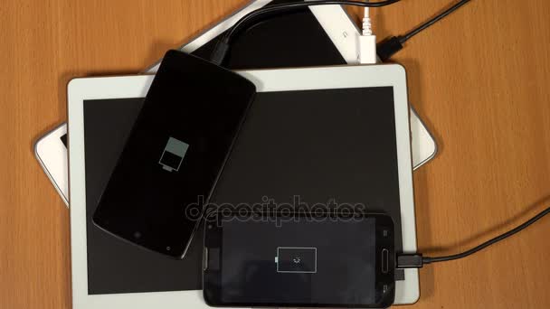 Tablet computadoras y teléfonos inteligentes cargando sobre fondo de mesa de madera — Vídeo de stock