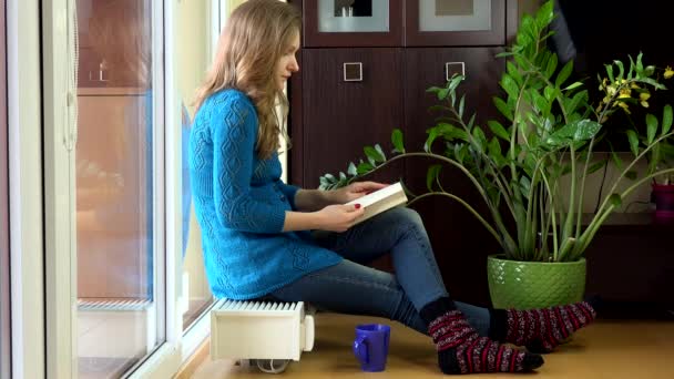 Прекрасная женщина читает книги и пьет кофе сидя на теплом радиаторе . — стоковое видео