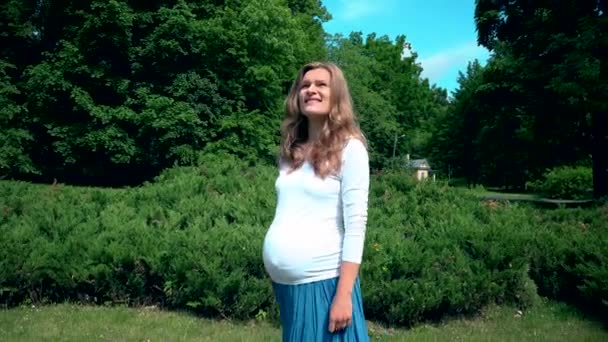 Schöne schwangere Frau, die im Park in der Sommersonne spaziert — Stockvideo