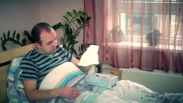 Hombre enfermo que sopla la nariz con un trapo acostado en la cama en casa. Temporada exacerbación de la alergia — Vídeos de Stock
