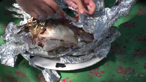 女性の手は、箔の屋外の暖炉の残り火で焼いた新鮮な魚をラップ解除します。4 k — ストック動画
