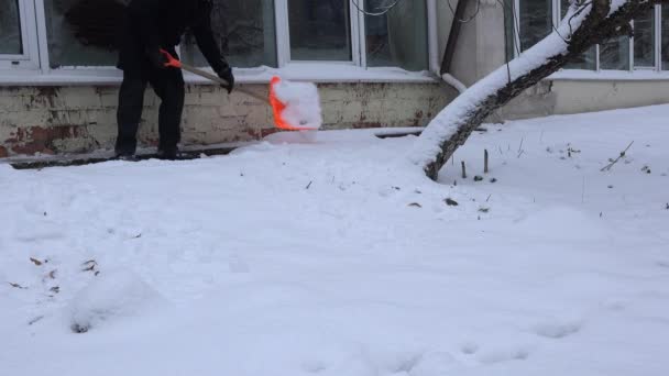Человек чистый снег с лопатой возле стены дома в зимнее время. 4K — стоковое видео