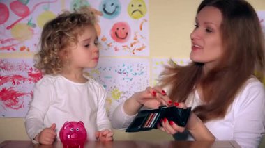 Genç anne ve sevimli kızı kumbara para koyarak.