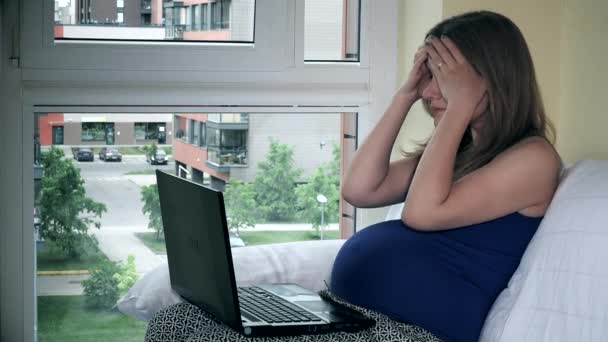 Уставшая фрилансер беременная женщина, работающая с ноутбуком, сидит у окна — стоковое видео