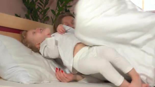 Непослушная смеющаяся девочка лежит рядом со своей матерью в постели — стоковое видео