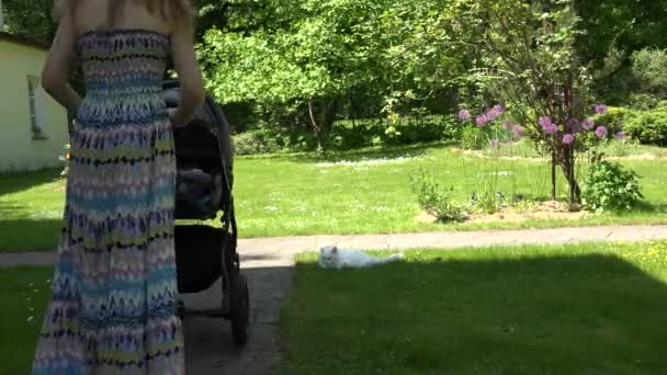 Mère en robe essayer d'envoyer bébé dormir dans la poussette dans le jardin. 4K — Video