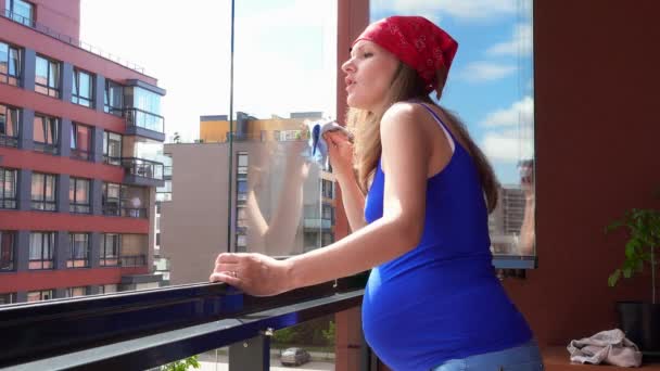 Mujer embarazada casa limpia de vidrio y mirar a través de la ventana en el balcón de la casa — Vídeo de stock