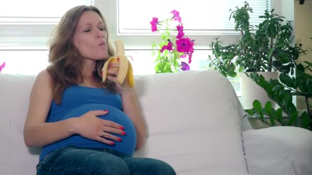 Счастливая будущая мама ест банановые фрукты и улыбается, глядя в камеру — стоковое видео