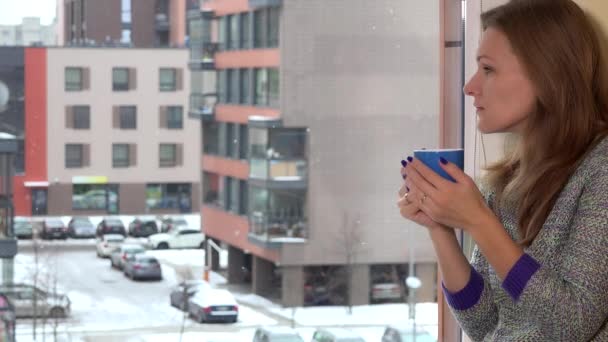 Mujer preocupada con taza de té de café sentado junto a la ventana. Copos de nieve nieve cayendo — Vídeos de Stock