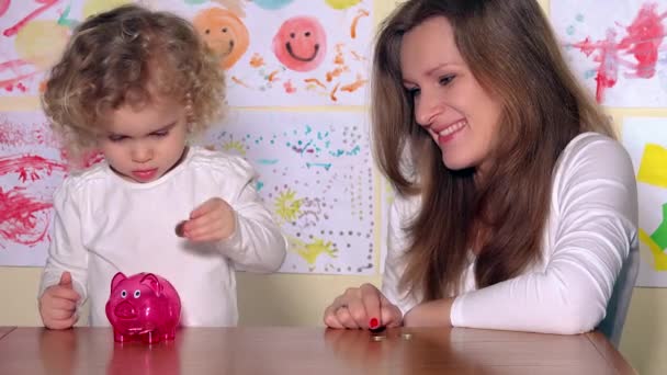 Woman with kid putting coins in piggy bank and show finger up looking at camera — Stock Video