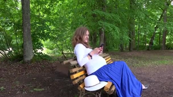 Pregnant female with smartphone sitting on park bench — Stock Video