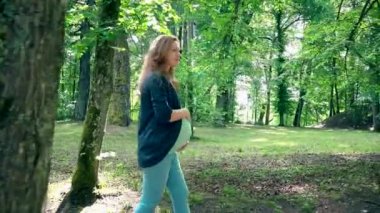 Dokuzuncu ay gebelikte mutlu hamile kadın Parkta yürümek ve güneş ışığı üzerinde gülümse