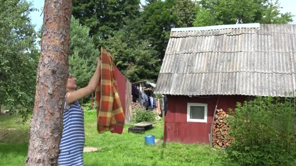 Жінка видаляє сухе обгортання для білизни з одягу в країні. 4-кілометровий — стокове відео