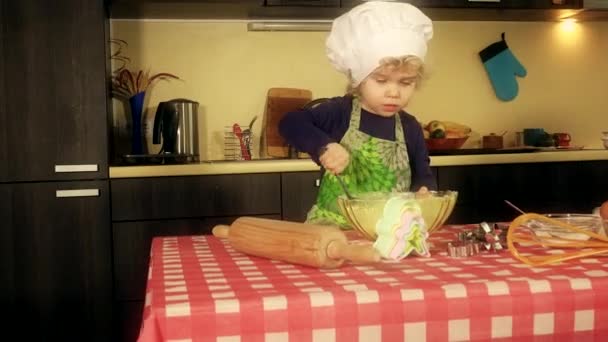 Mignonne mini chef fille avec chapeau de cuisinier et tablier mélange farine préparation désert — Video