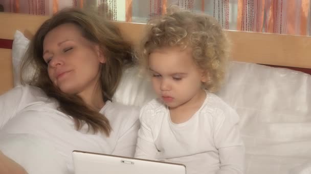 Belle fille enfant regardant tablette pendant que la mère dort au lit — Video