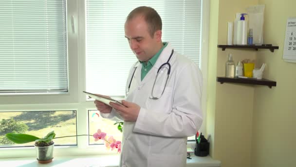 Arts met de stethoscoop met behulp van digitale tablet tegen venster in ziekenhuis kabinet — Stockvideo