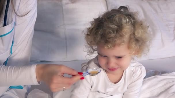 Ženský lékař dát lžíci sirupu nemocné holčičky sedící v posteli — Stock video